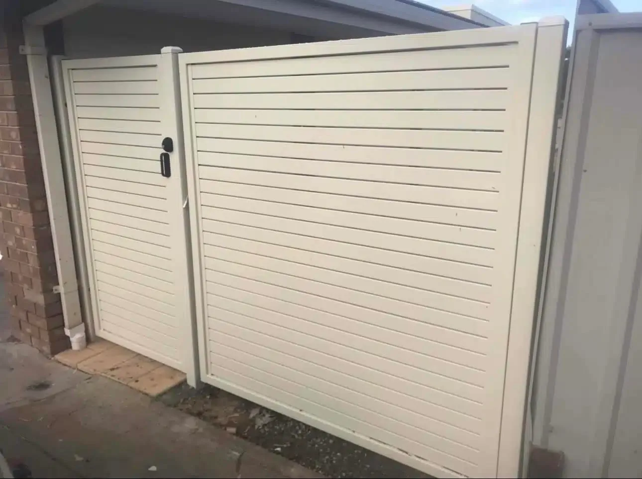 Cream horizontal-slat pedestrian gate beside a garage