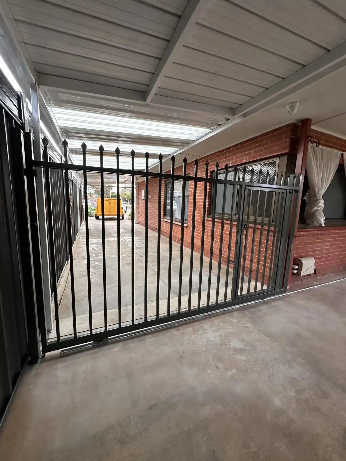 Black steel swing gate at the end of a covered carport