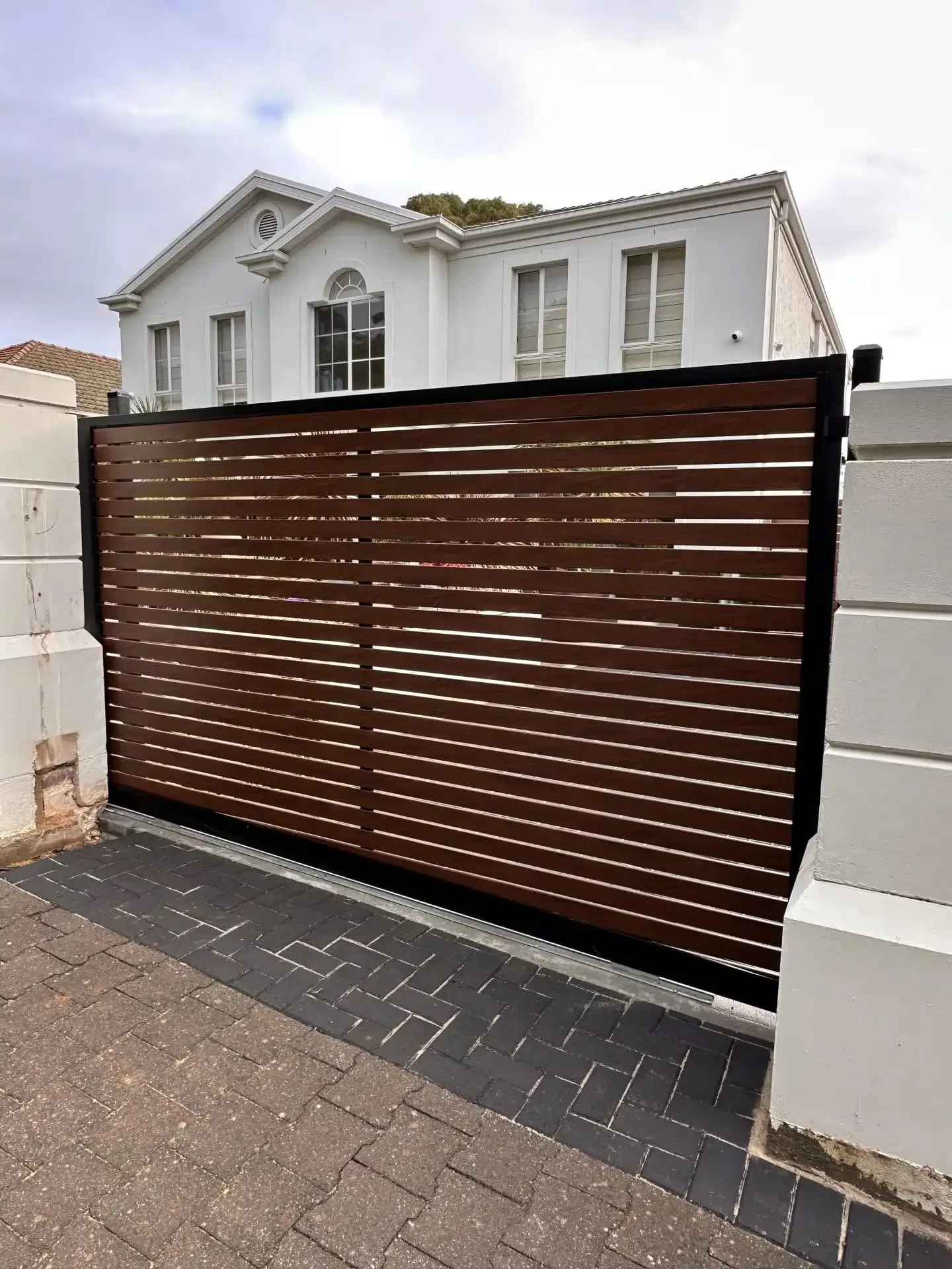Timber-look slat automatic sliding gate in front of a two-storey home