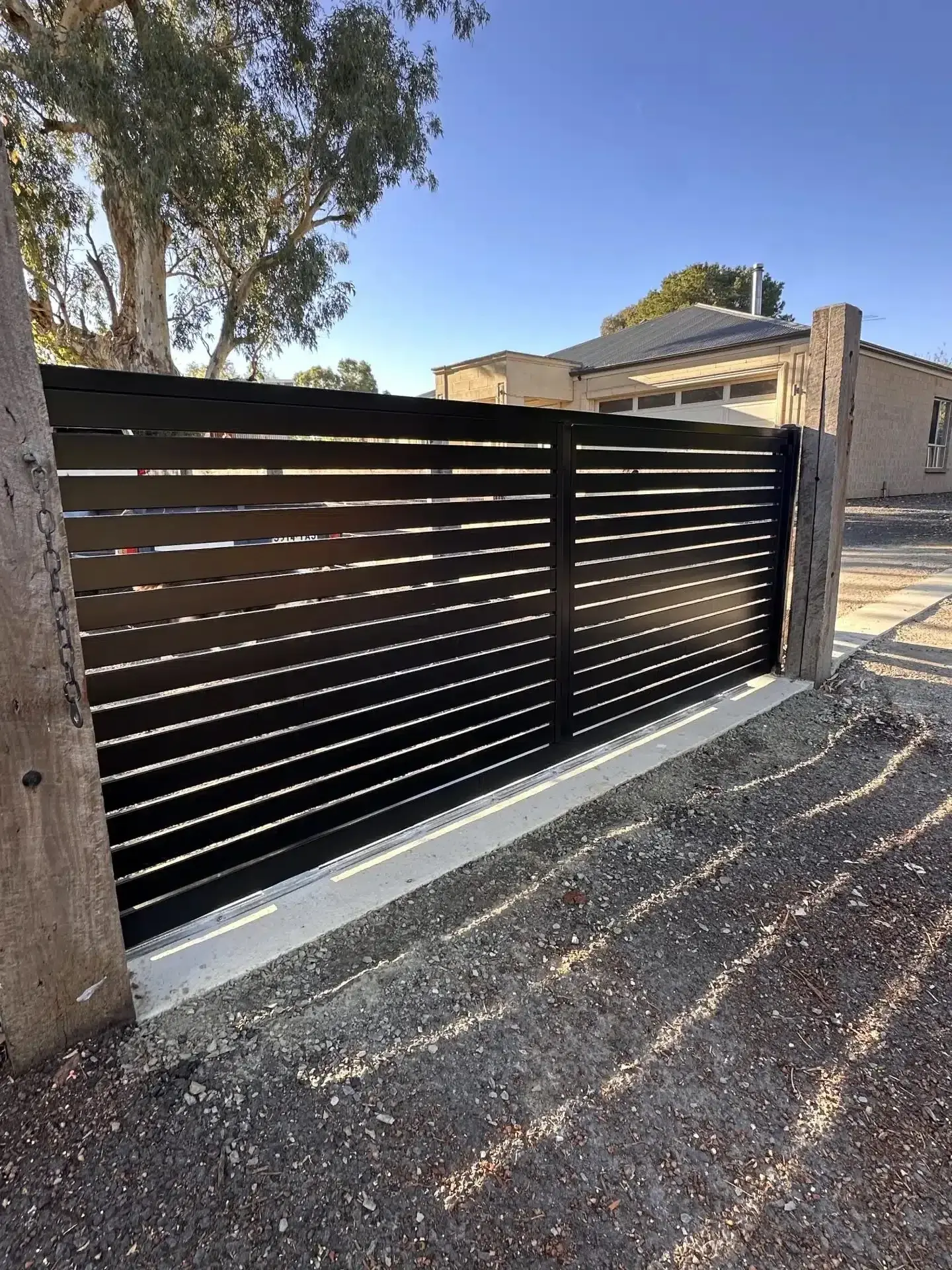 Black horizontal-slat automatic sliding gate on a gravel driveway
