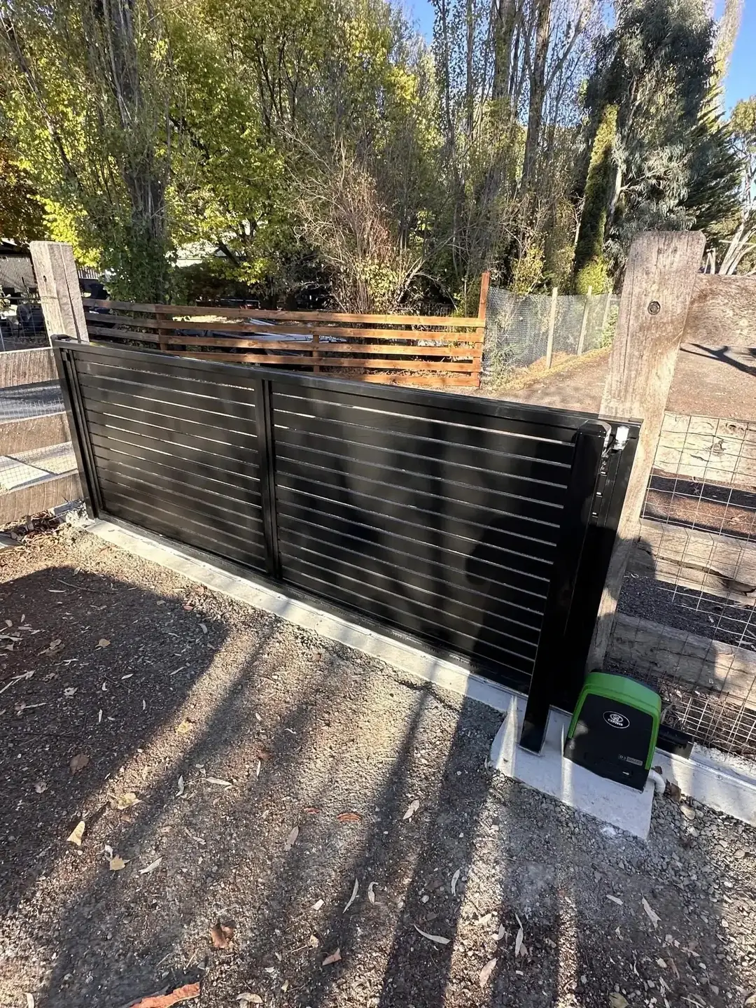 Black slat sliding gate with its gate motor beside the driveway