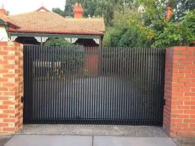 Black vertical-slat driveway gate between red brick piers