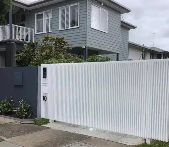 White vertical-slat automatic sliding gate in front of a weatherboard home