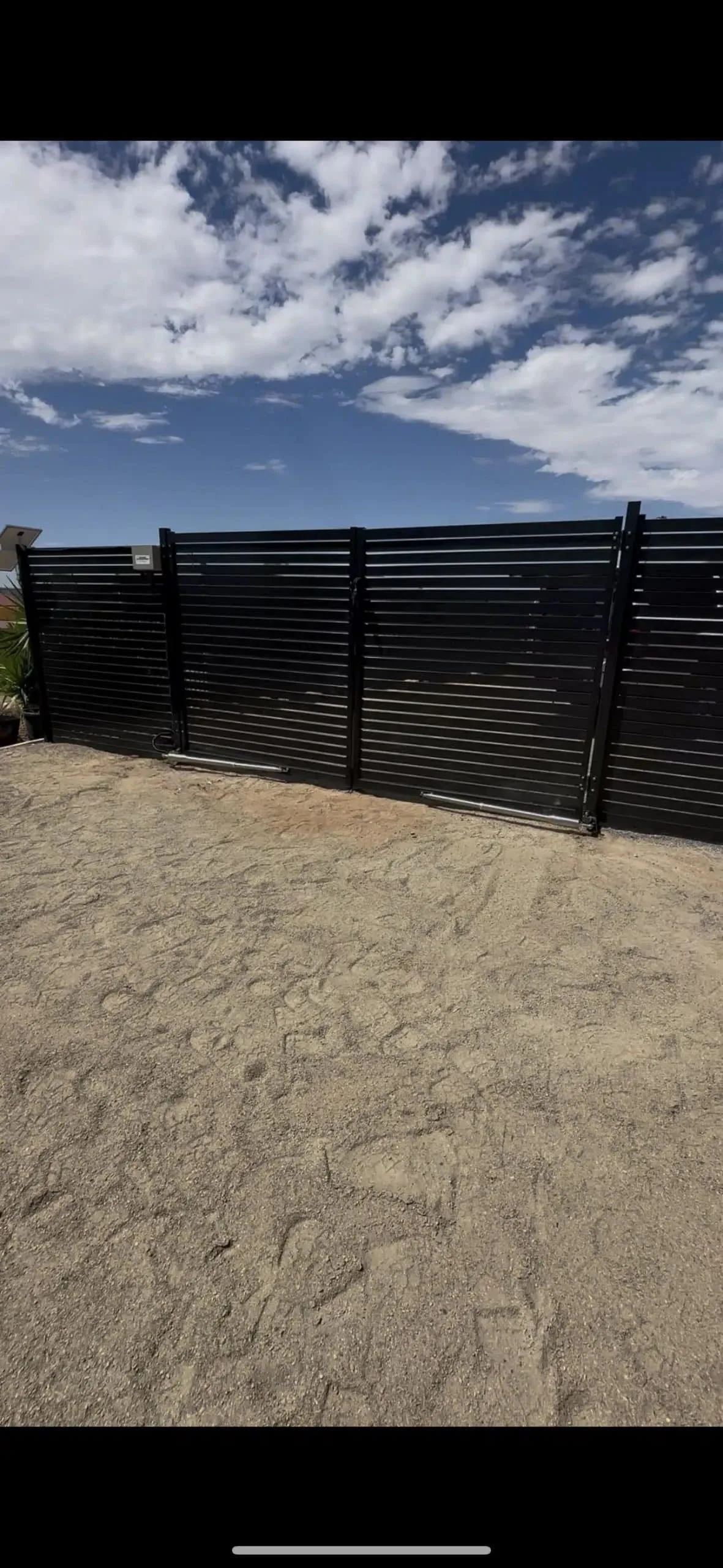Black automatic gate across a sandy rural driveway