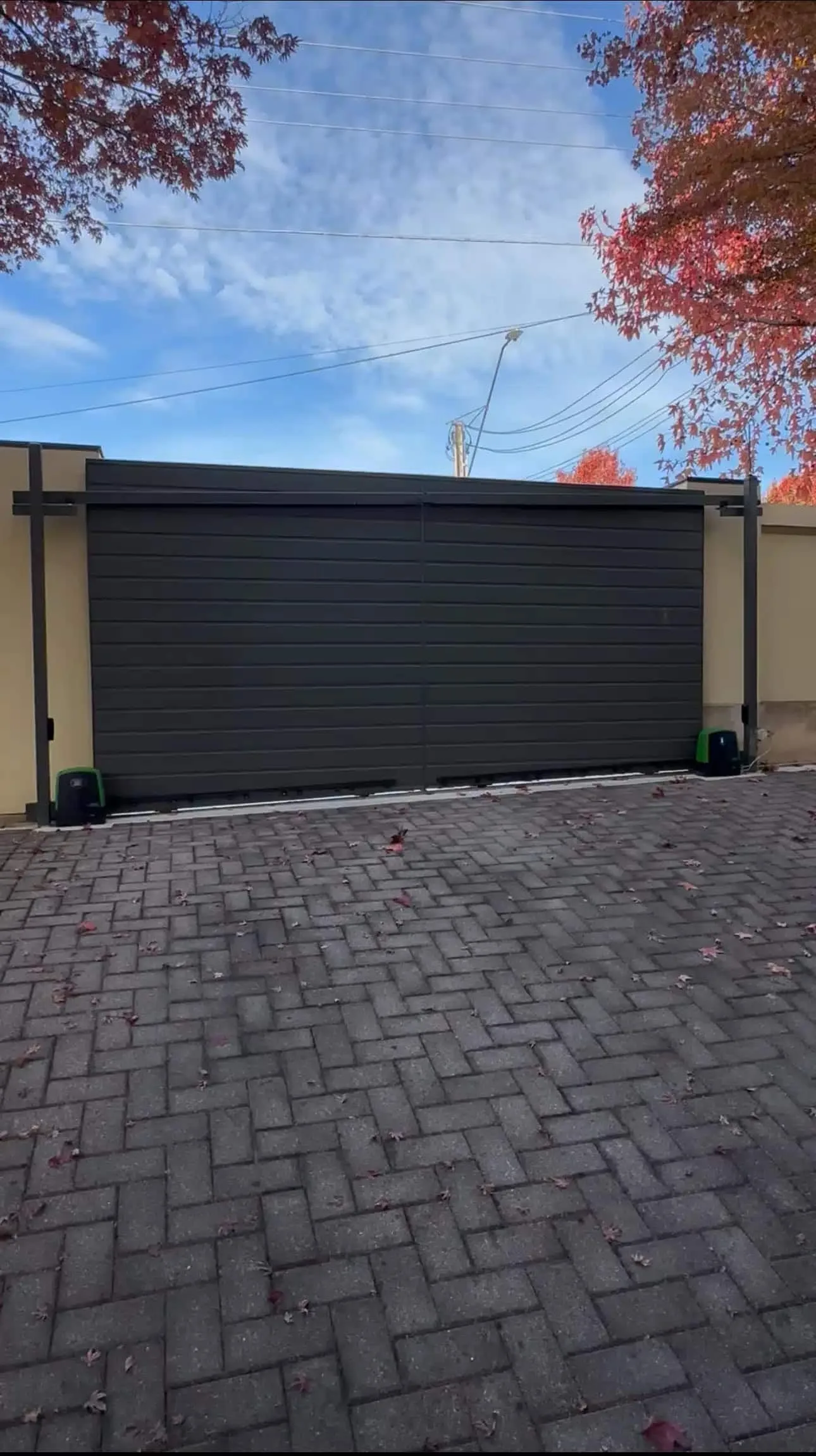 Black automatic sliding gate across a brick-paved driveway