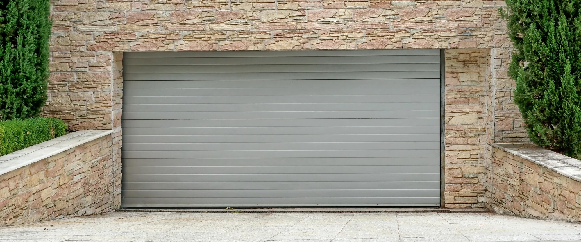 Grey automatic garage-style door set in a stone wall