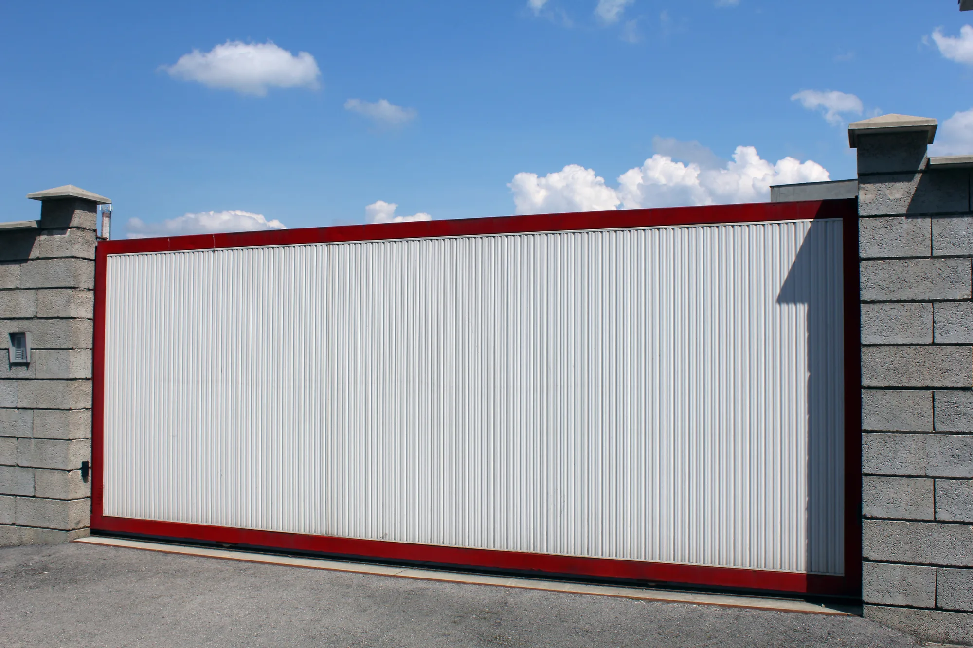 White electric sliding gate with a red frame between stone piers