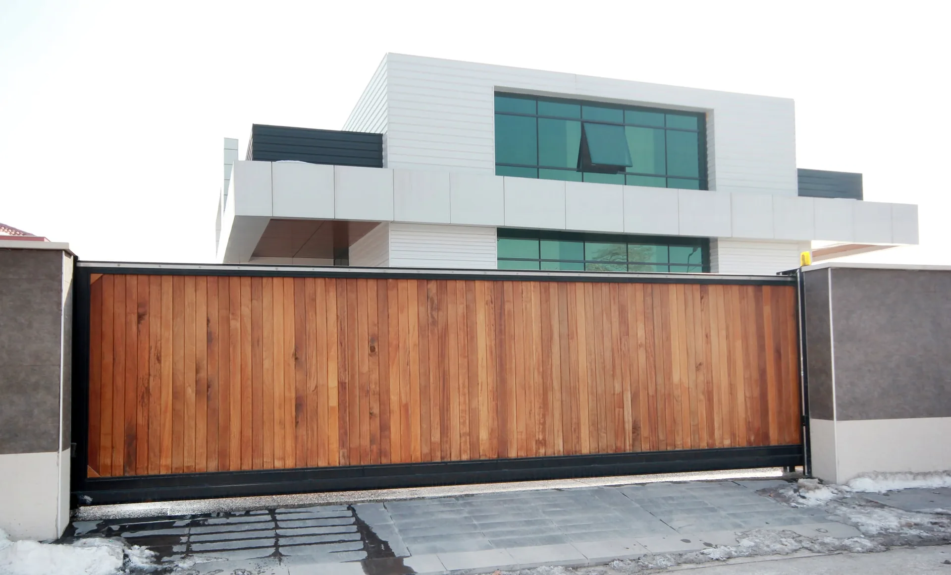 Timber-panel automatic sliding gate in front of a modern white building
